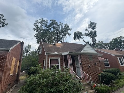 Brick home with storm-damaged trees and roofline